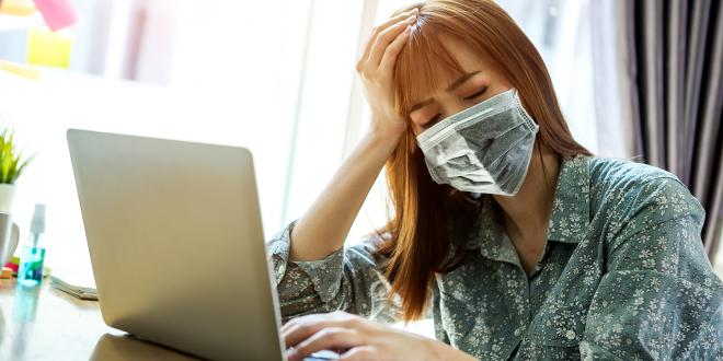 a fatigued woman in a mask working from home